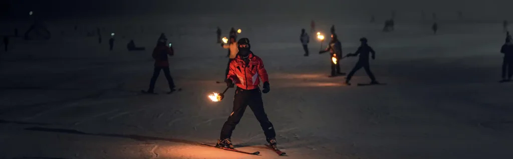 Night skiing experience in US - Night skiers holding torches at Nightskii Adventure Travel Resort.